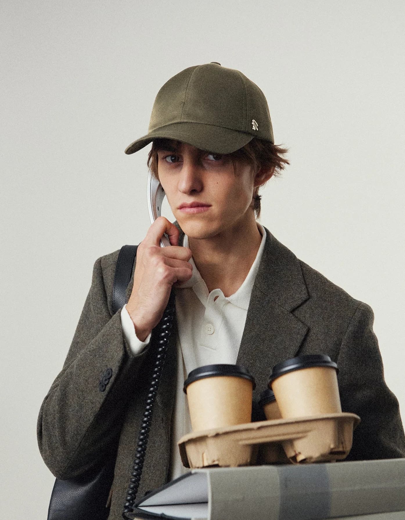 A person in a tailored coat and cap holding a tray of coffee cups