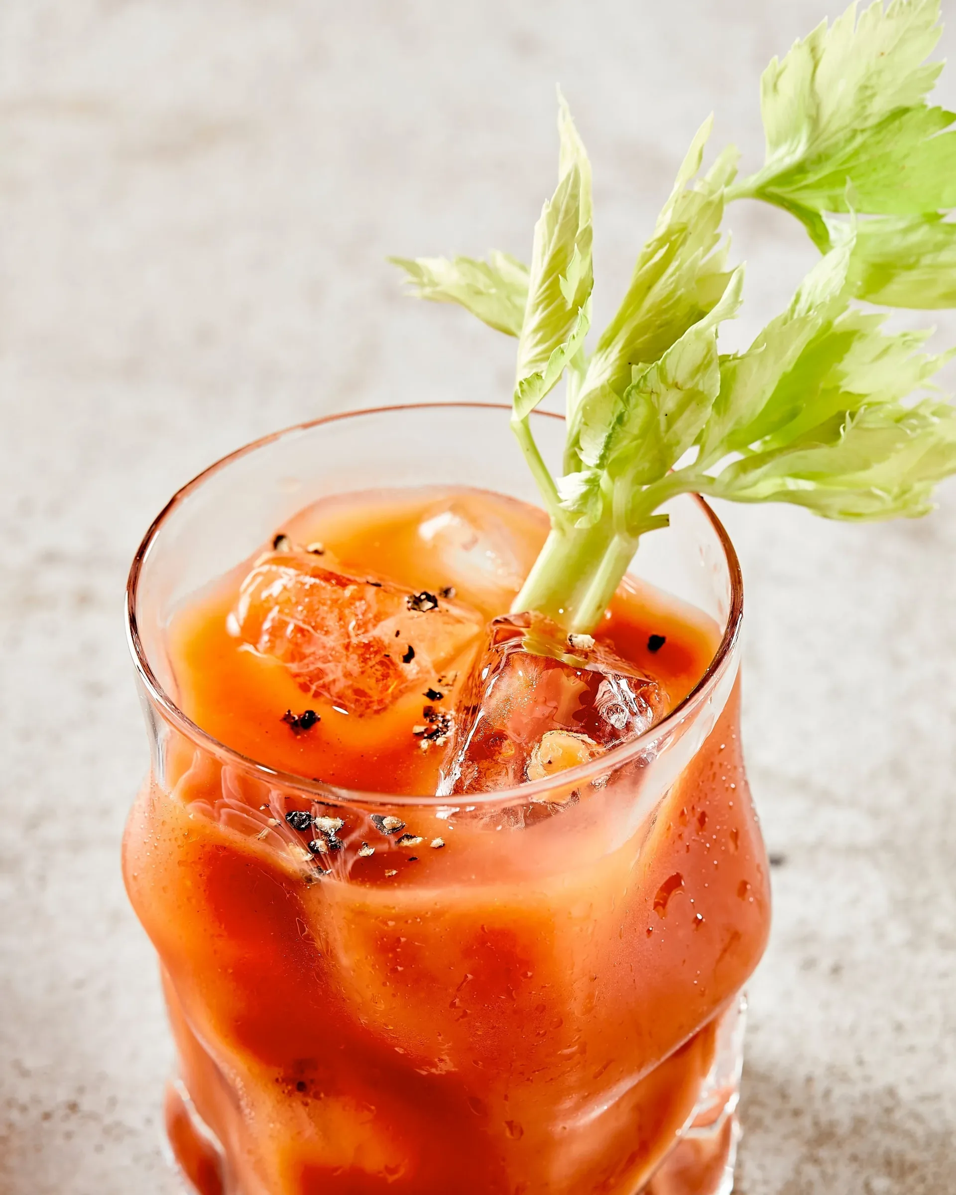 A chilled tomato-based drink with celery, photographed on a pale stone surface