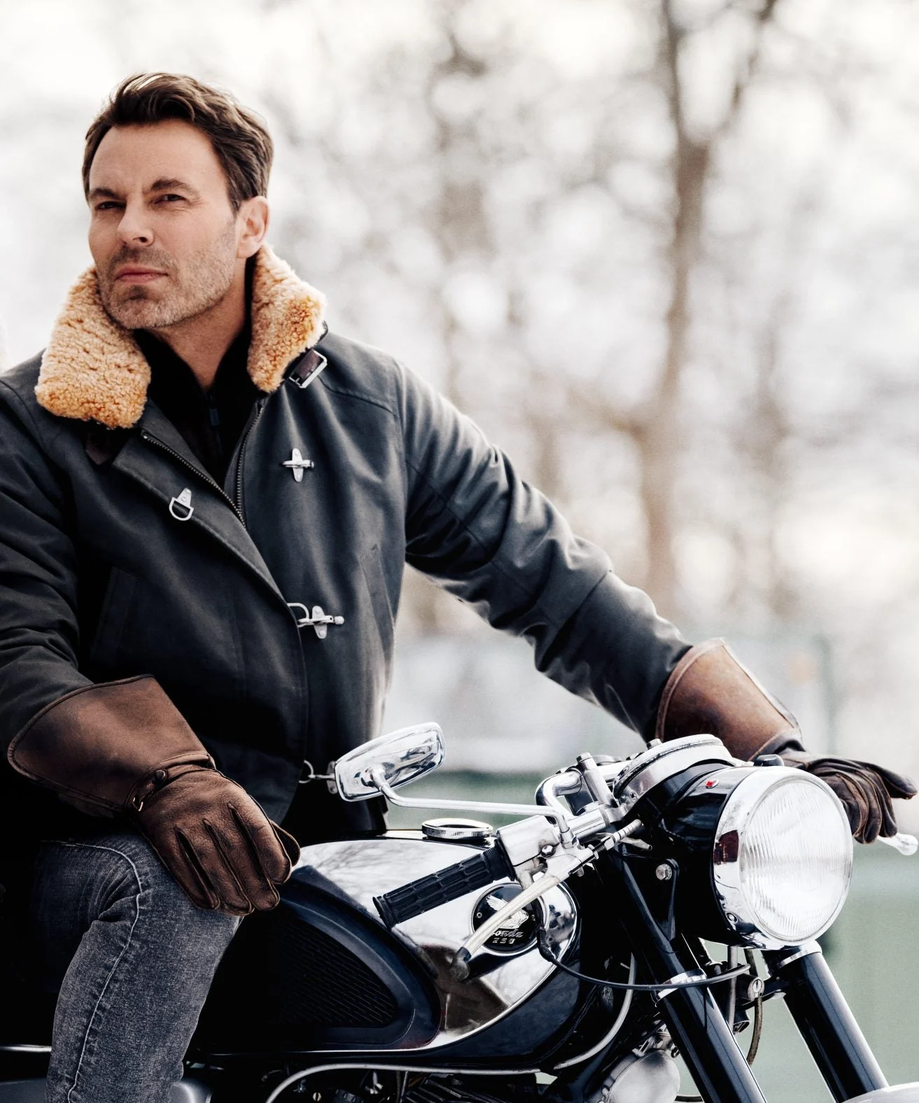 Detail of a shearling-collared jacket and gloved hands on a motorcycle