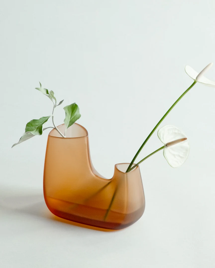 A frosted amber vessel holding a cutting, photographed against a pale ground