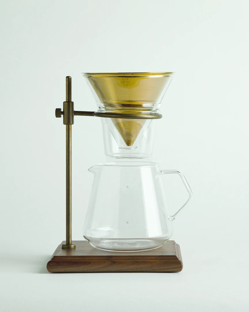 A brass-stand pour-over brewer above a glass carafe