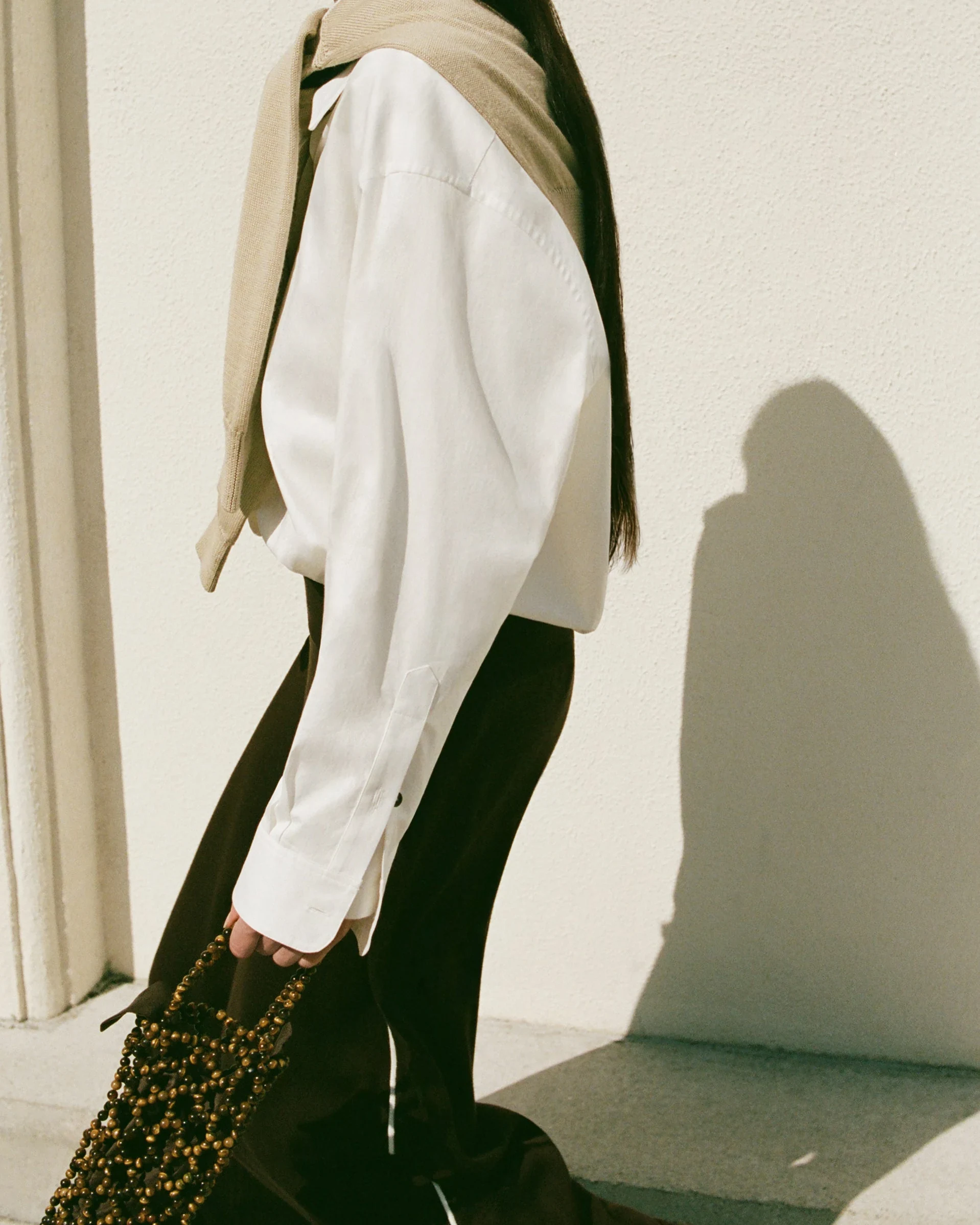 A figure in a white shirt and dark trousers carrying a woven bag