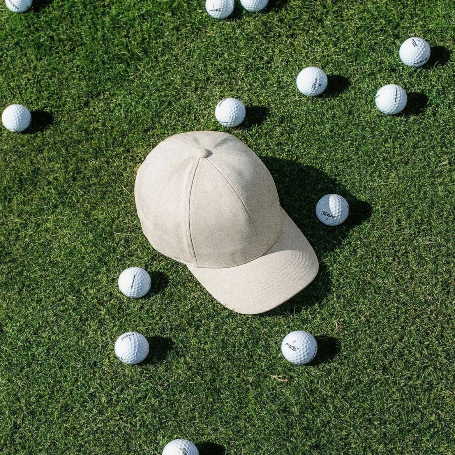A pale cap placed on grass among scattered golf balls