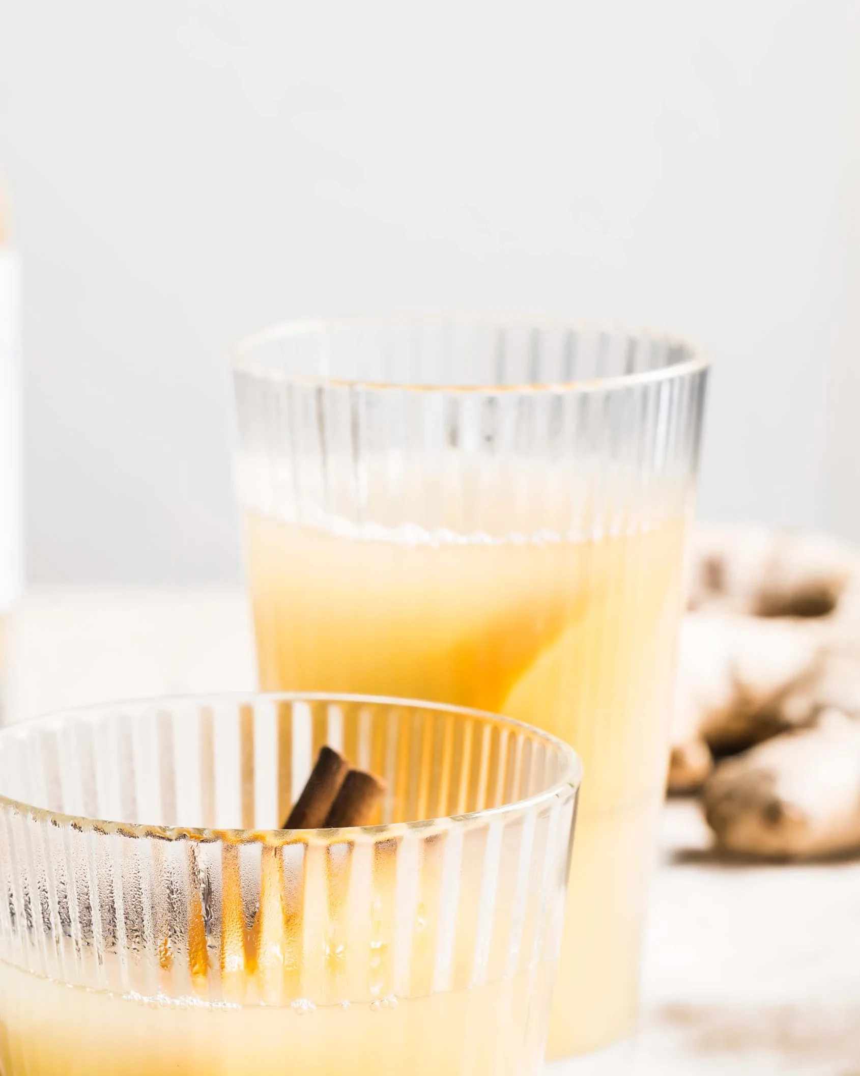 Two ribbed glasses holding a pale citrus drink with cinnamon